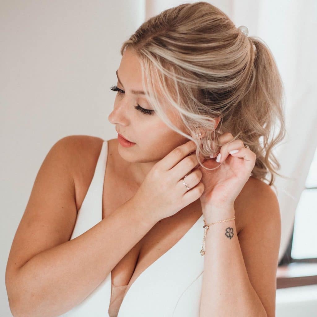 bride with swept up hair by Marci Knuth Hair And Makeup LLC putting her earrings in