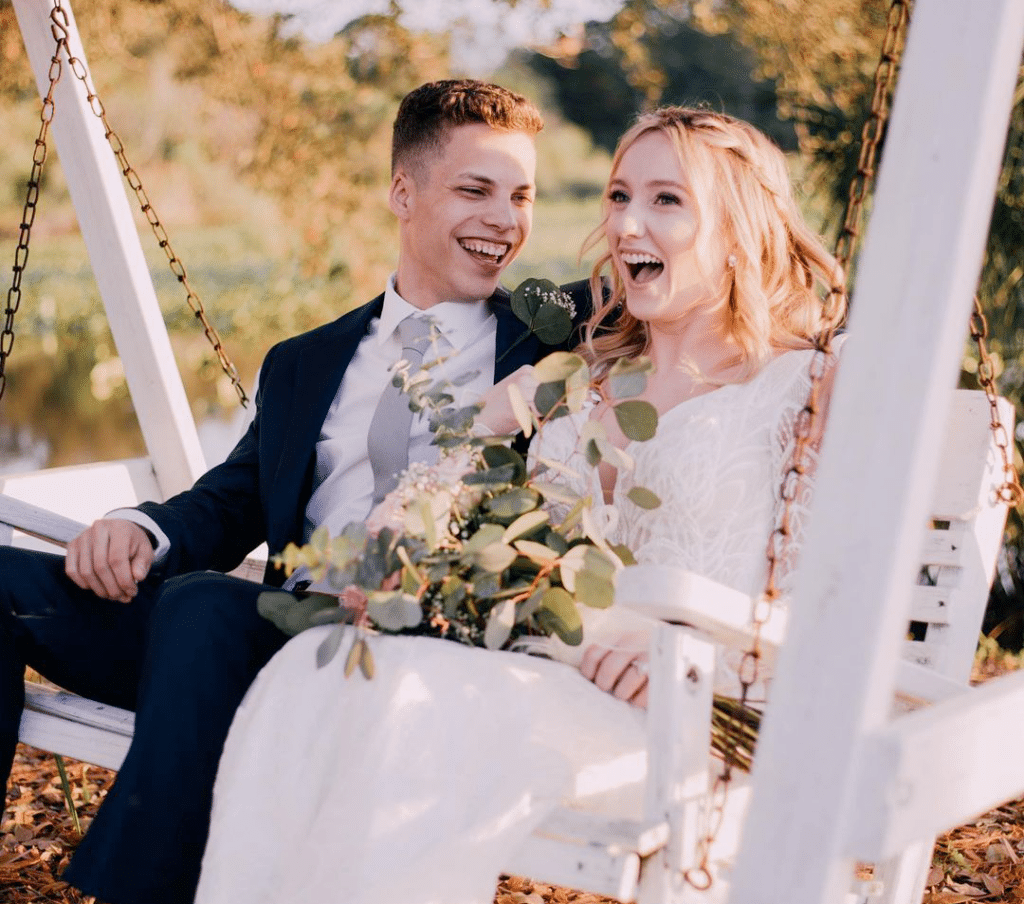 bride and groom sitting in a wooden swing and laughing together at the Rocking L Ranch Wedding Barn