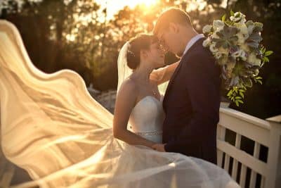 Bride and groom sharing a romantic sunset moment at St. Johns Golf and Country Club in St. Augustine Florida, with the bride's veil flowing dramatically in the wind as golden light filters through the trees