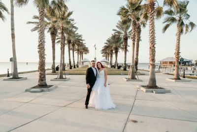 bride and groom standing on palm lined walkway at the beach near 520 on the Water