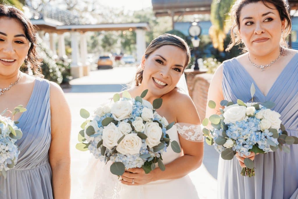 bride holding bouquet of white flowers and pale blue hydrangeas by Dream Designs Florist with bridesmaids in hydrangea blue dresses