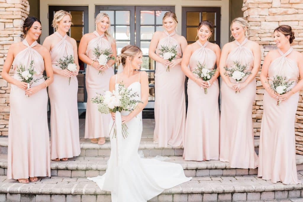 bride on stairs with bridesmaids in blush smiling at her at St. Johns Golf & Country Club