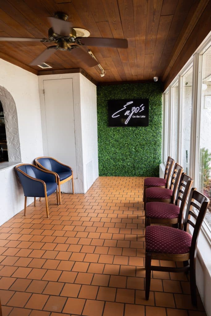 entrance to enzo's on the lake in florida with greenery wall, sign, brick floor, and leather chairs