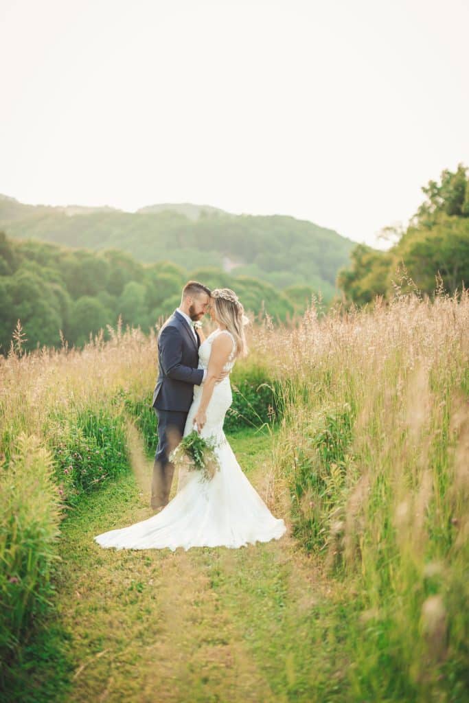 bride and groom on path cut in meadow with hills in the background photographed by Slone Photography, LLC