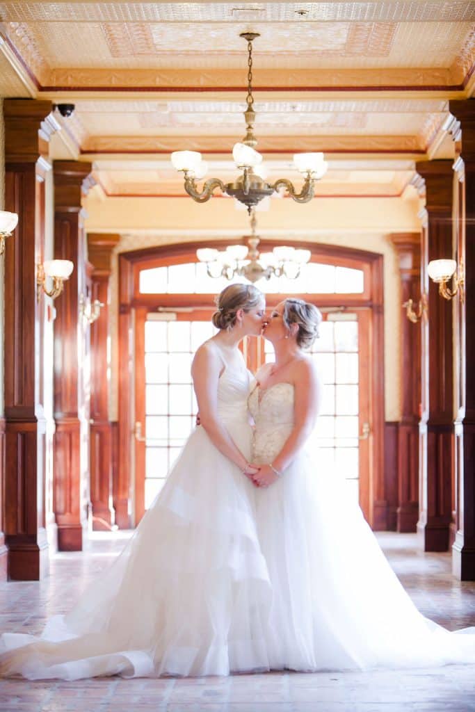 brides kissing in long hallway photographed by Hundreds of Moments Photography