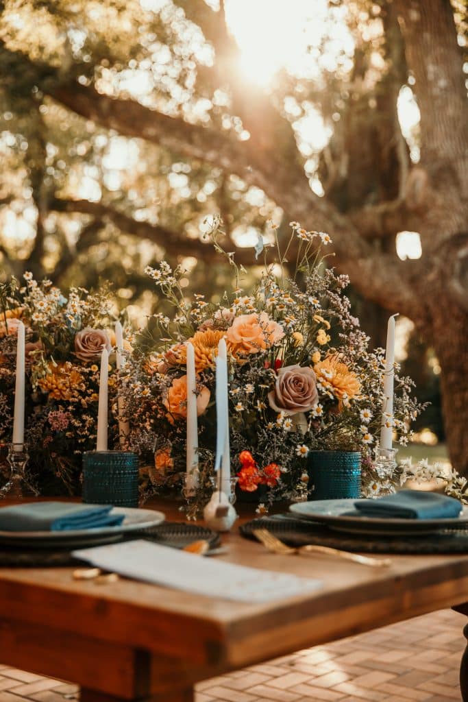 Tablescape outdoors on a long wooden table, white candles, teal napkins and beautiful florals down the middle in Orlando, FL