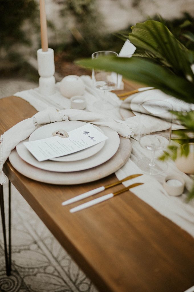 wooden table with white charges and gold and white cutlery from Echo Event Rentals
