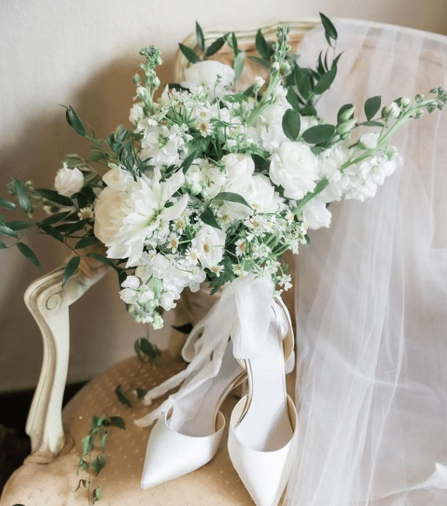 White floral bouquet with beautiful greenery, rested on a chair with wedding shoes and a veil.