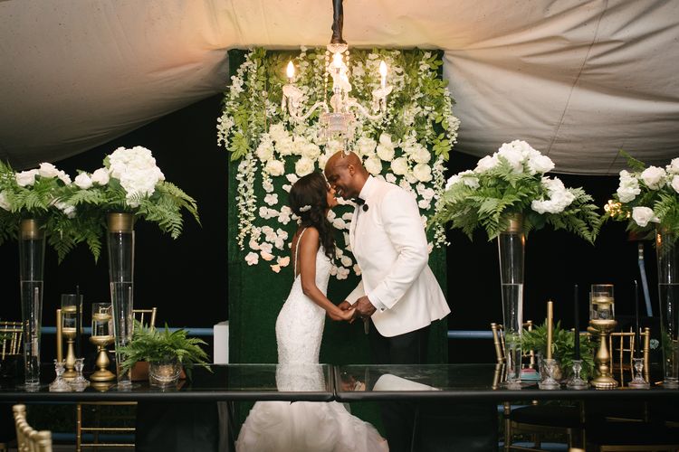 bride and groom kissing in front of greenery chandelier and tall table centerpieces at reception coordinated by A. Marie Events & Design