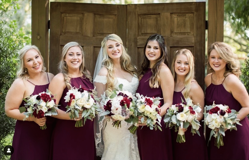 wedding party in burgundy dresses with the bride, all holding floral bouquets that highlight red and burgundy flowers, Orlando, FL