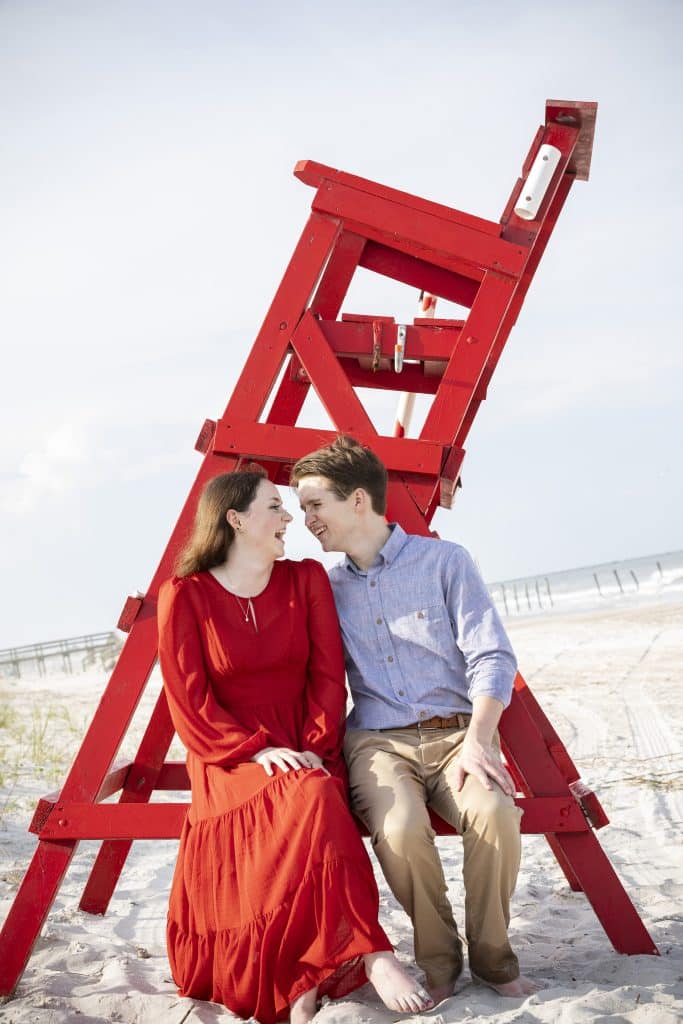 engagement photo of couple sitting on red lifeguard chair at beach photo by Evan Hampton Photography