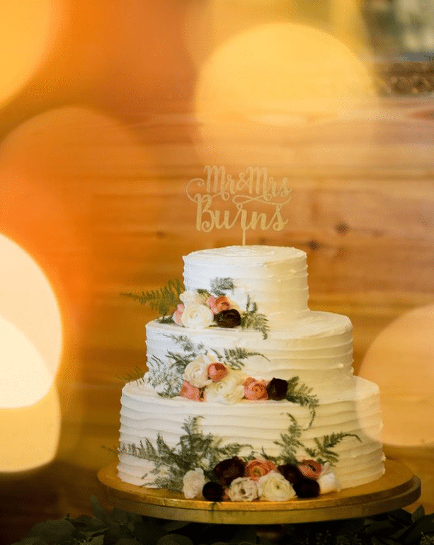 3 tiered wedding cake with white frosting and each layer has florals added for design, by Laynie Botanicals