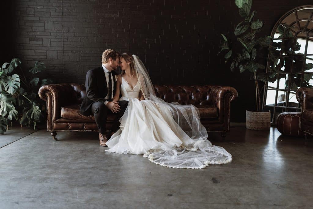 bridal portrait by Torontali Photography an Orlando wedding photographer of couples on a brown leather couch in front of a black brick walls with cement floor