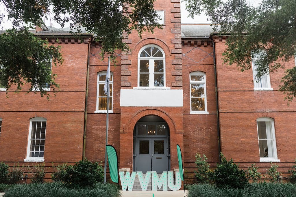 brick school house building with big wvmu marquee letters in front of it and two tall ground flags that are green