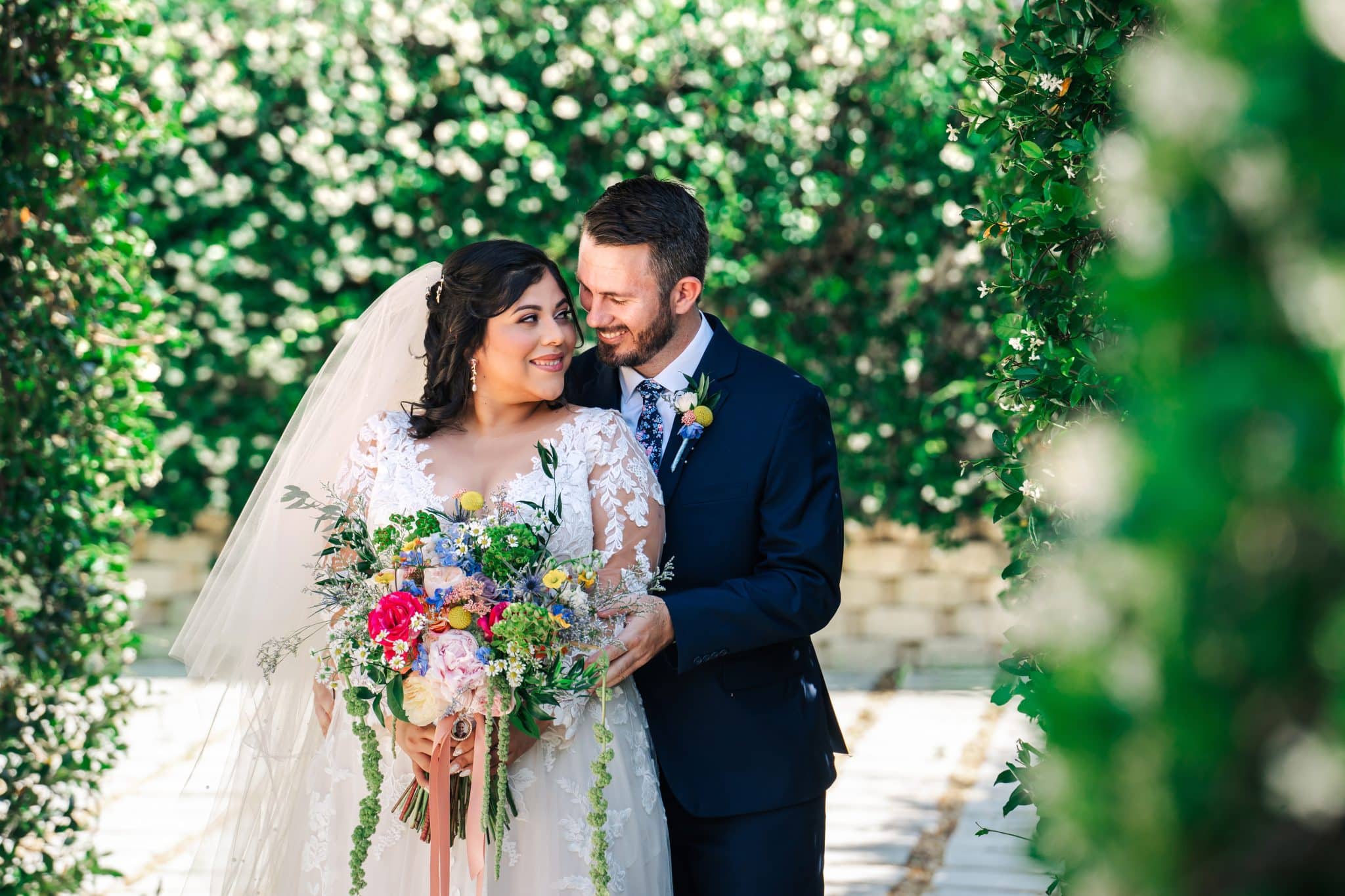 Newlyweds pose together under a garden archway with colorful flower bouquet in whimsical wedding at Hidden Barn Venue in Apopka, FL