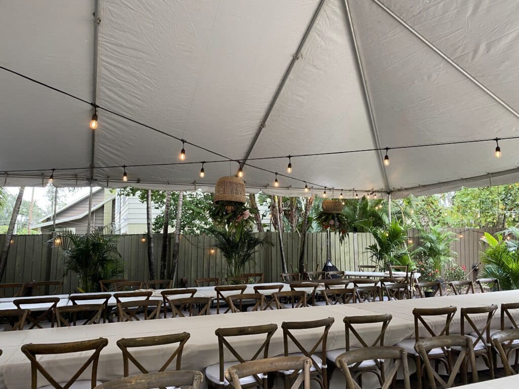 Long table with a white tablecloth under a tent with string lights and wooden chairs, Central, FL
