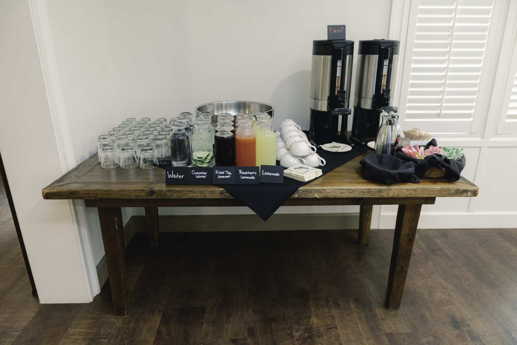 wooden table with containers of drinks setup with coffee ups and glasses 