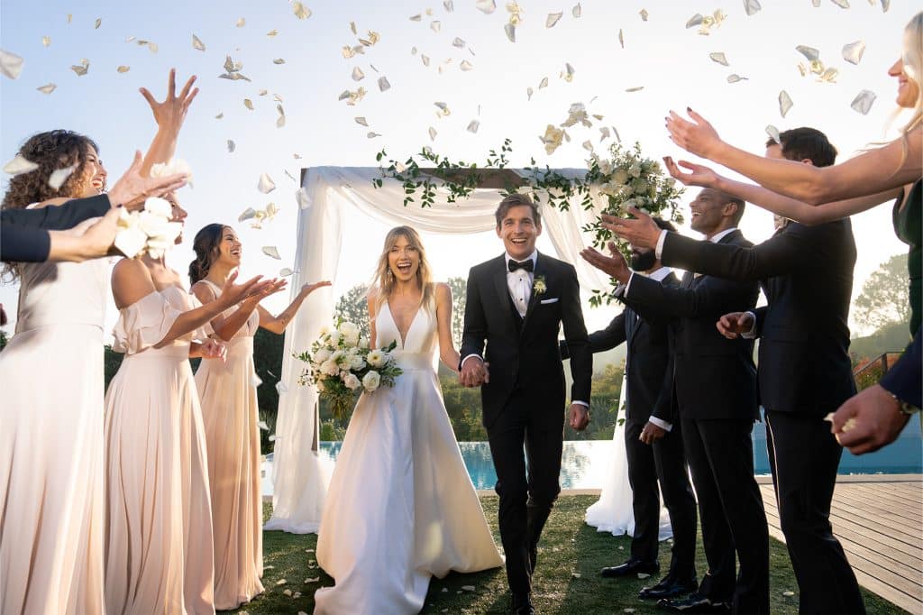 Couple leaving their ceremony, with wedding party tossing flower petals, outdoors on the beach, Generation Tux