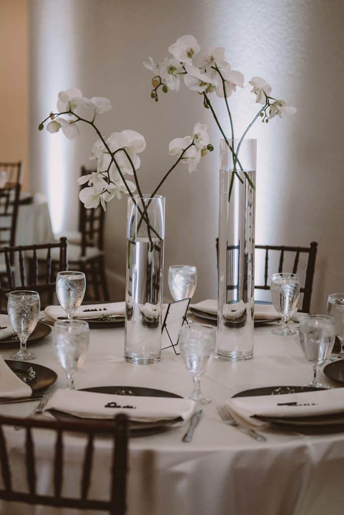 simple table set up, black chairs, white table cloths, clear glass ware, tall, thin vases with single stem white flowers, Central FL