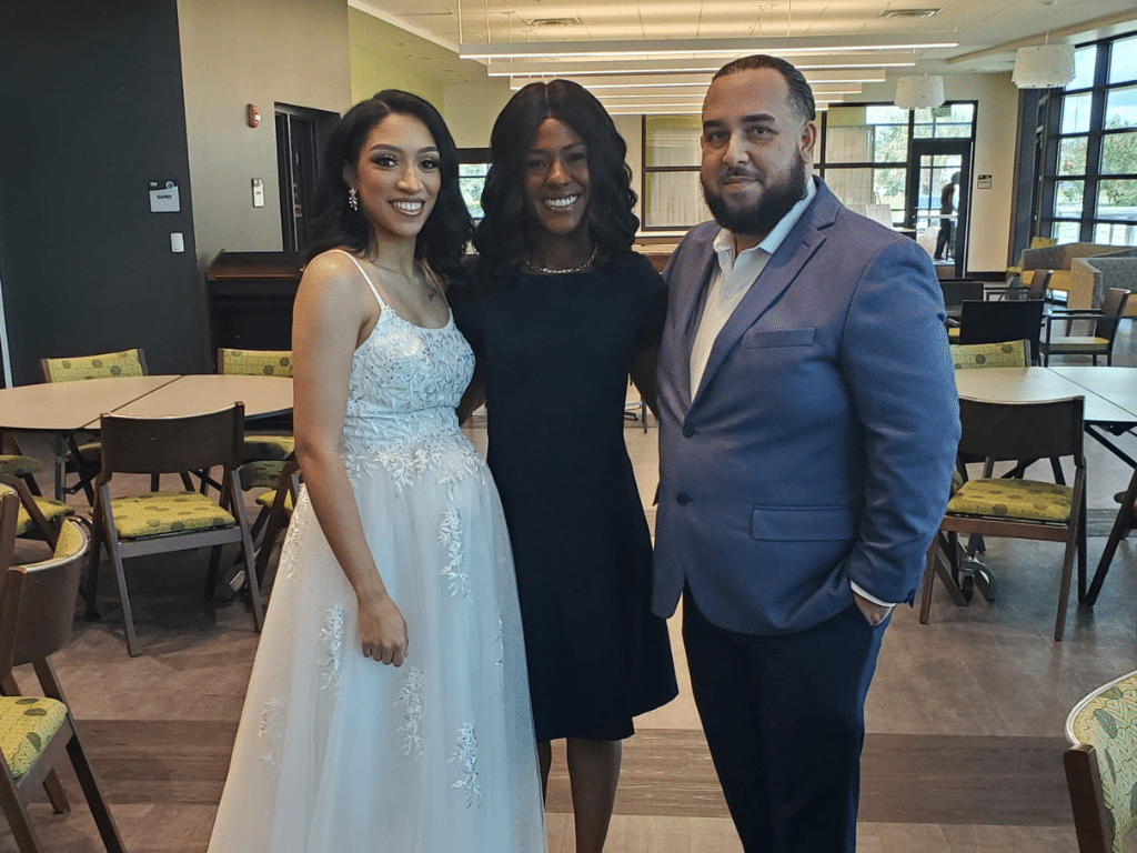 Wedding couple standing with their wedding planner indoors, bride in a white dress, groom wearing a grey/blue jackets and dark pants, planner is in a black cocktail dress, Central FL