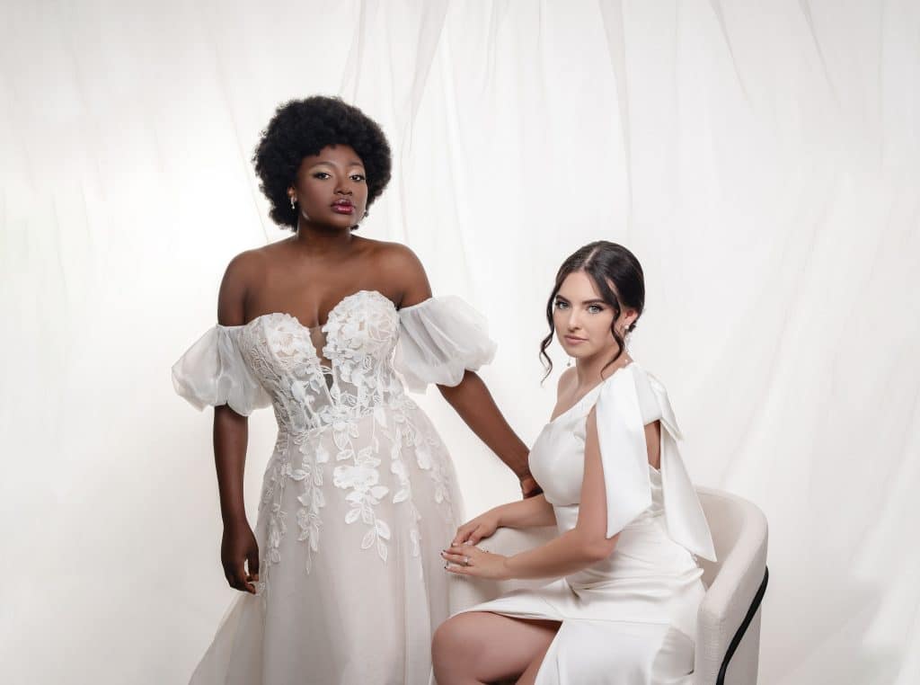 Two brides in white, one standing, one sitting on a white chair, with a white backdrop, Haley Finegan Hair and Make Up, Central FL