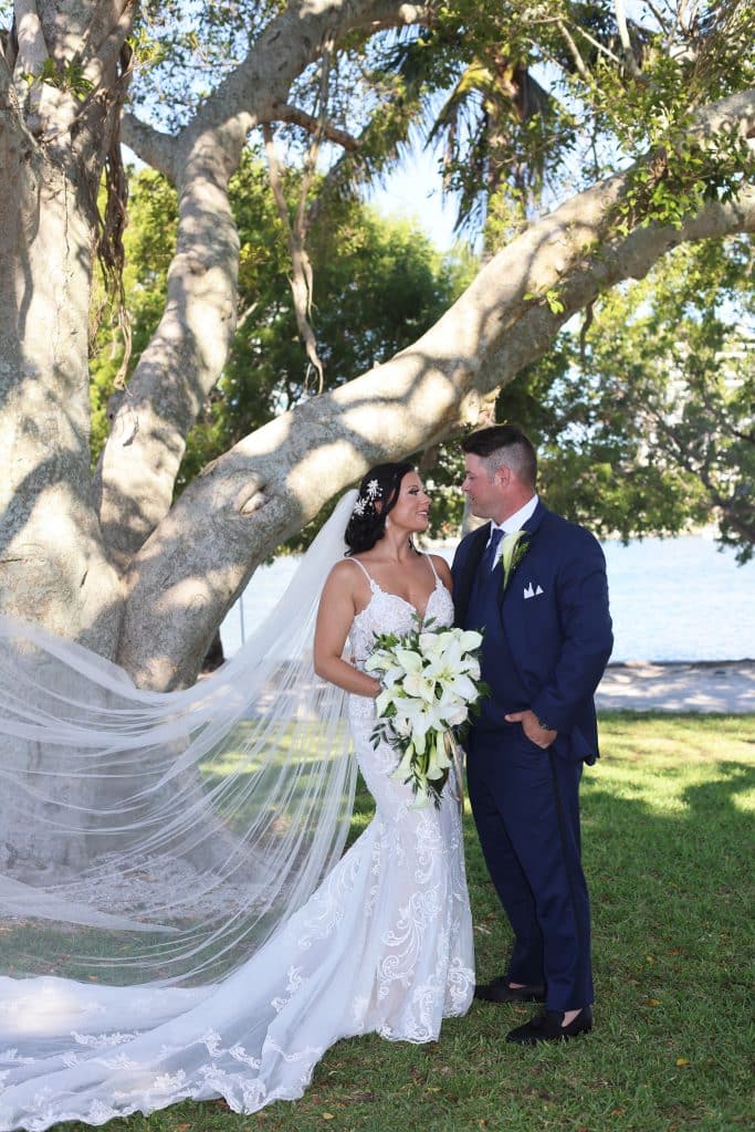 Bride and groom gazing into each other's eyes, under a beautiful tree with her flowing veil and blue sky, Central FL