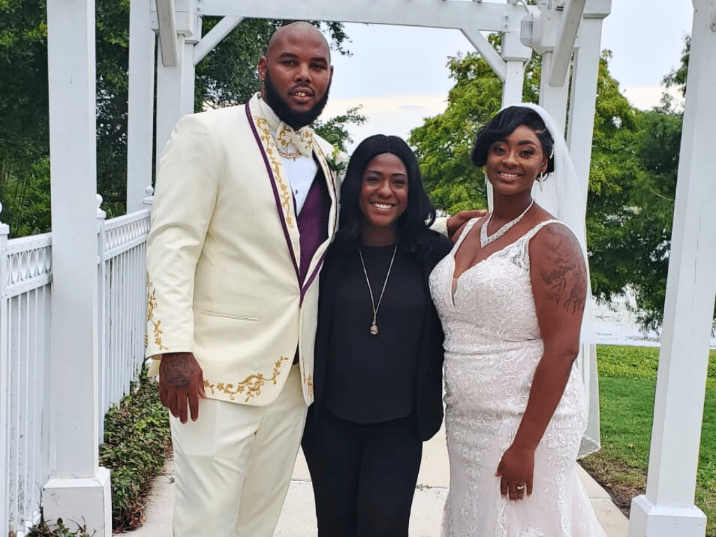 Wedding couple with their officiant in black, couple in a white dress and officiant white suit, lined with maroon, Central FL
