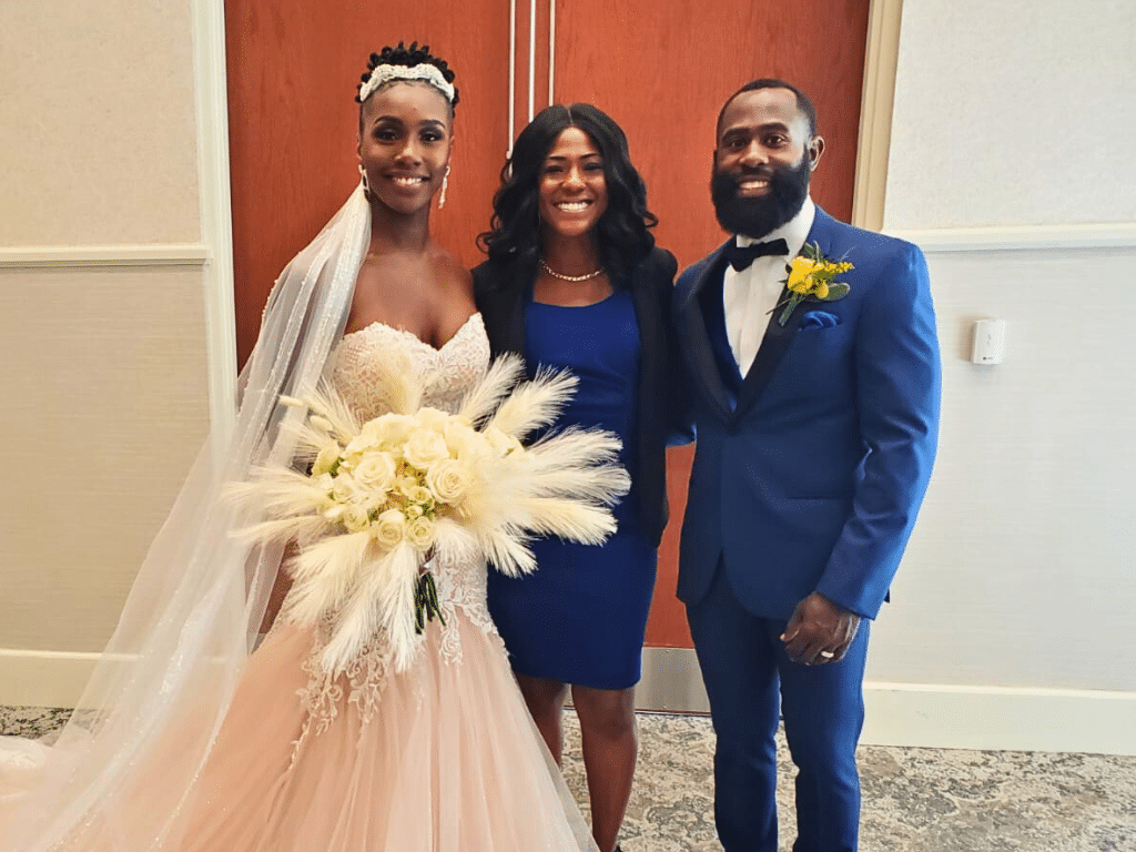 Couple with their officiant on their wedding day, groom in a blue suit, officiant in a blue dress, bride wearing white with a large bouquet of white and yellow flowers with feathers, Central FL