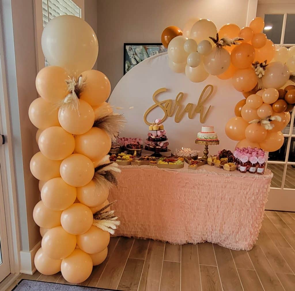 birthday party for Sarah with peach colored balloons in a tower, a peach table covering to the floor, white backdrop with 