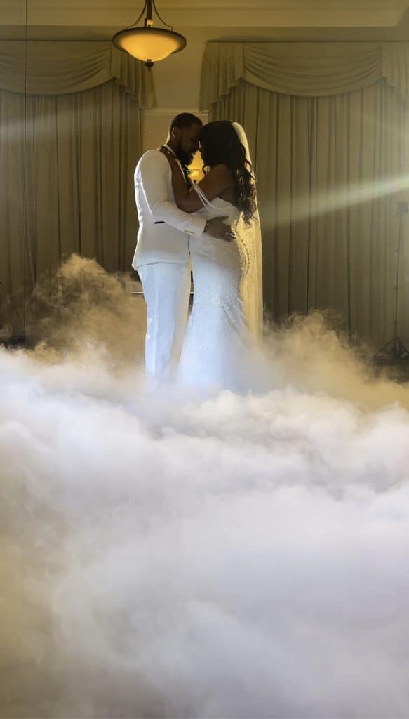 Couple in all white, dancing to their first dance, with light smoke in the foreground, Kwik Entertainment
