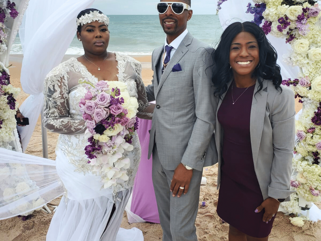 Wedding couple with their officiant, who is wearing a dark purple dress, bride in her white dress with a white head piece and bouquet of white, purple and lavender flowers, Central FL