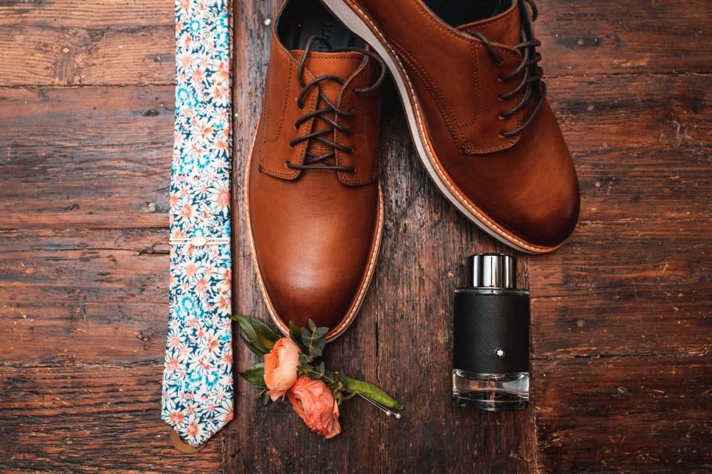 Flatlay of a man's brown leather shoes on the right, vibrant colored tie on the left, the peach boutonniere below the shoes accompanied by a bottle of cologne, Uptown Selfies, Central FL