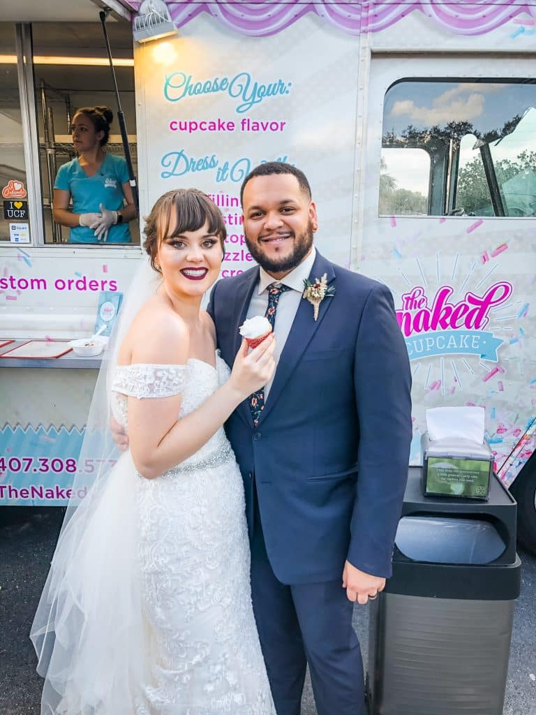 Couple holding a cupcake in front of the Naked Cupcake truck on their wedding day, Central, FL