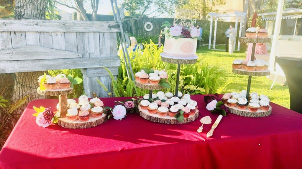 Dessert table of cakes and cupcakes on a red tablecloth, outdoors, Bells Cake House, Central FL