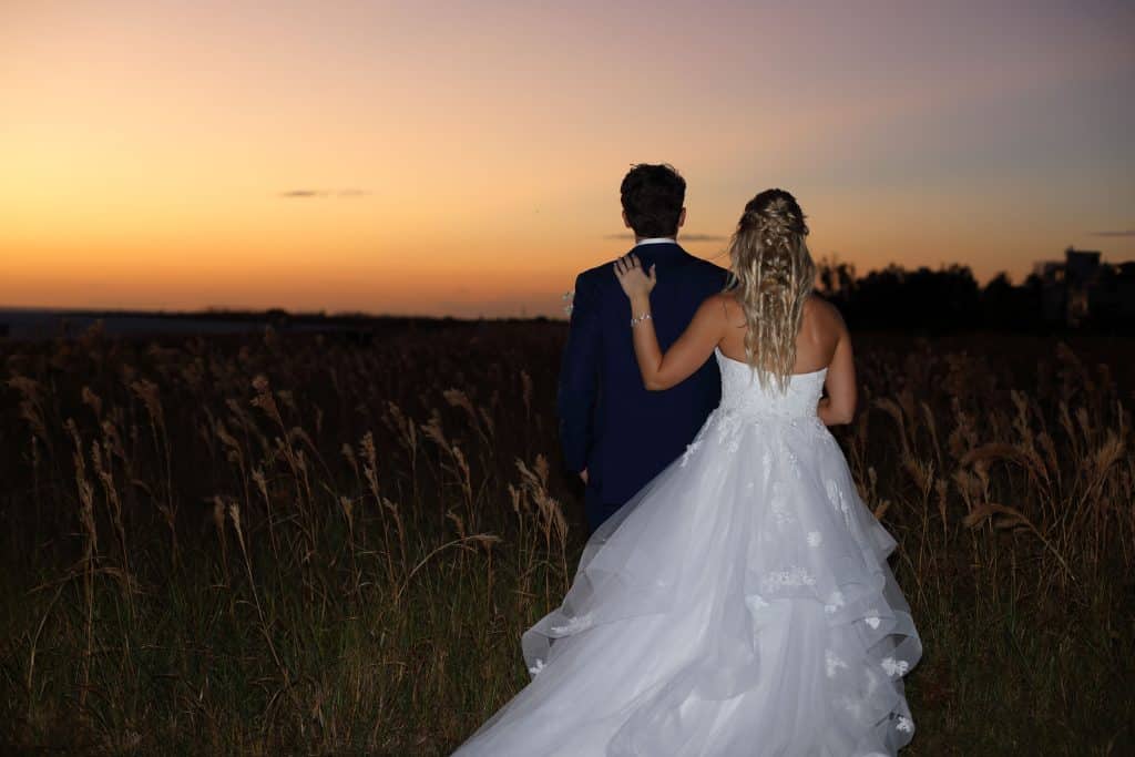 Wedding couple in a field, facing a sunset, the bride's left hand on the groom's shoulder, JVK Photography, Central FL