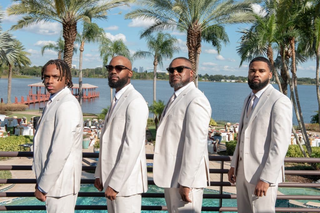 Wedding party dressed in light grey suits on a balcony with the water in the background, JB's Cinematic Creations and Photography