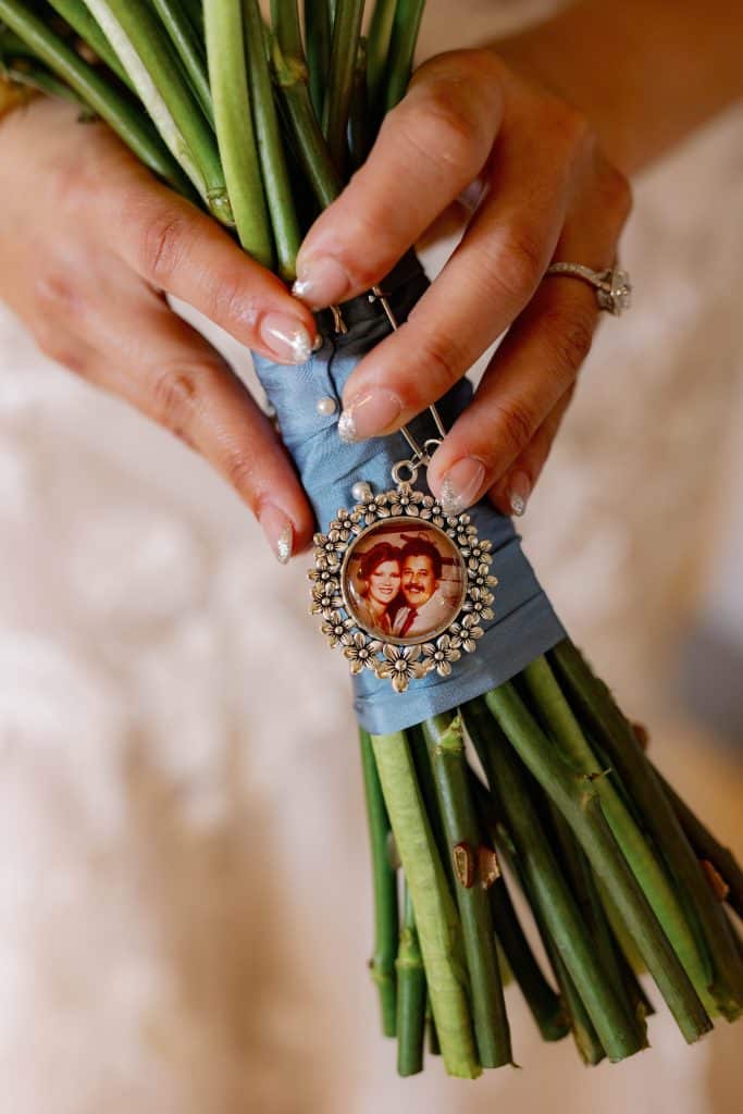 Close up of the stems of a bride's bouquet, blue ribbon accented with a circular framed photo of her parents, JF Events and Flowers