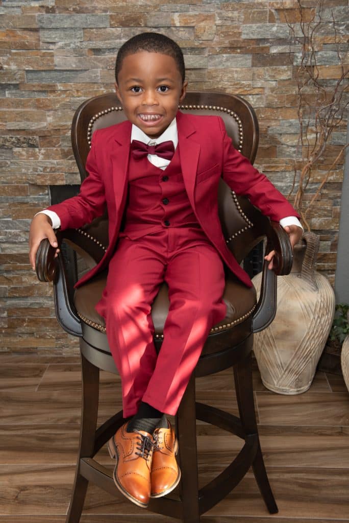 Young boy dressed in red suit sitting on a chair, smiling for the camera, central FL
