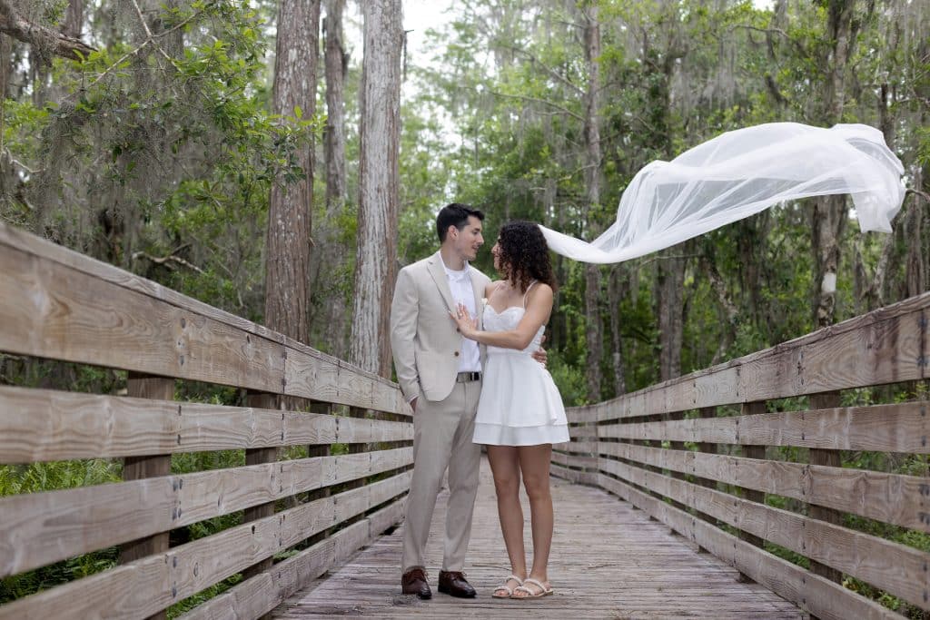 Couple on a wooden bridge in the woods, facing each other, with her white veil blowing in the breeze, Central FL