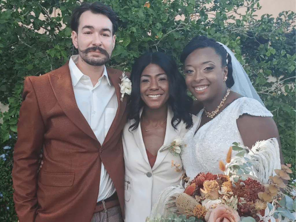 Bride and groom posing with their celebrant, groom wearing brown suit, bride in a white dress, celebrant wearing a white suit with a brown top, Central FL