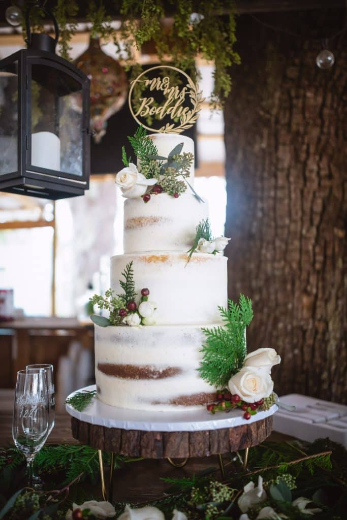 Four tiered cake, adorned with greenery, on a wooden cake stand, with a Mr & Mrs sign on top, Central, FL