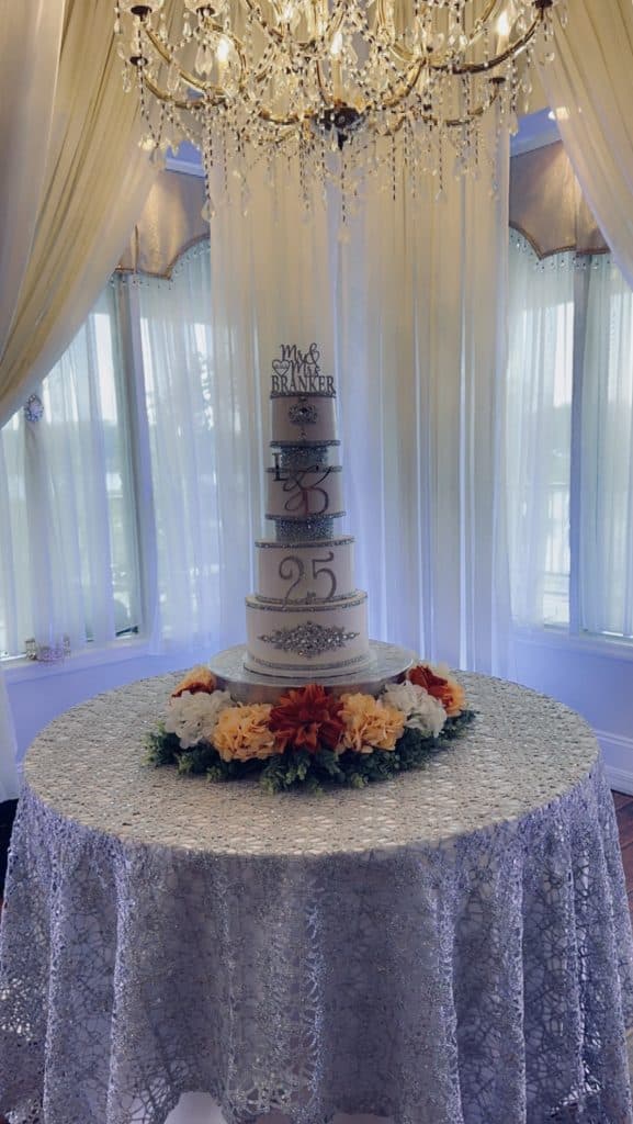 25th anniversary cake with four tiers, surrounded by vibrant flowers at the base, 25 written on the cake in silver along with silver borders for each tier, Bells Cake House, Central Fl