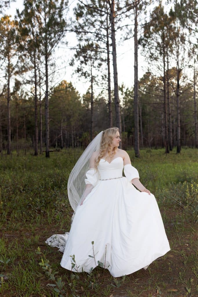 Bride wearing her large flowing strapless dress in the grass, outdoors, surrounded by trees, Central FL