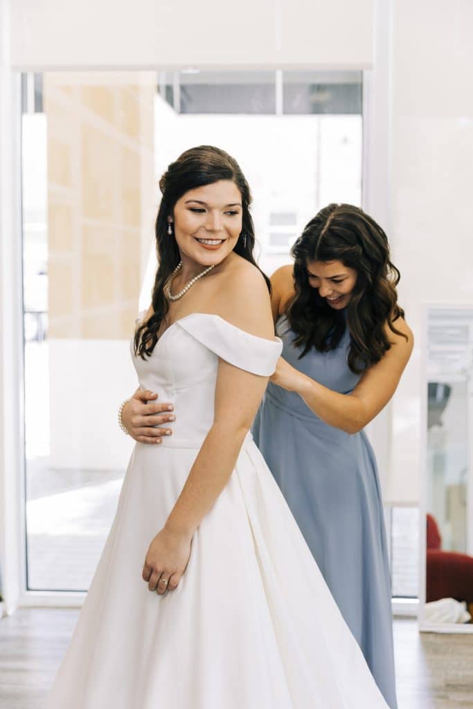 a bridesmaid helping the bride with her dress as they prepare for her wedding, Central FL