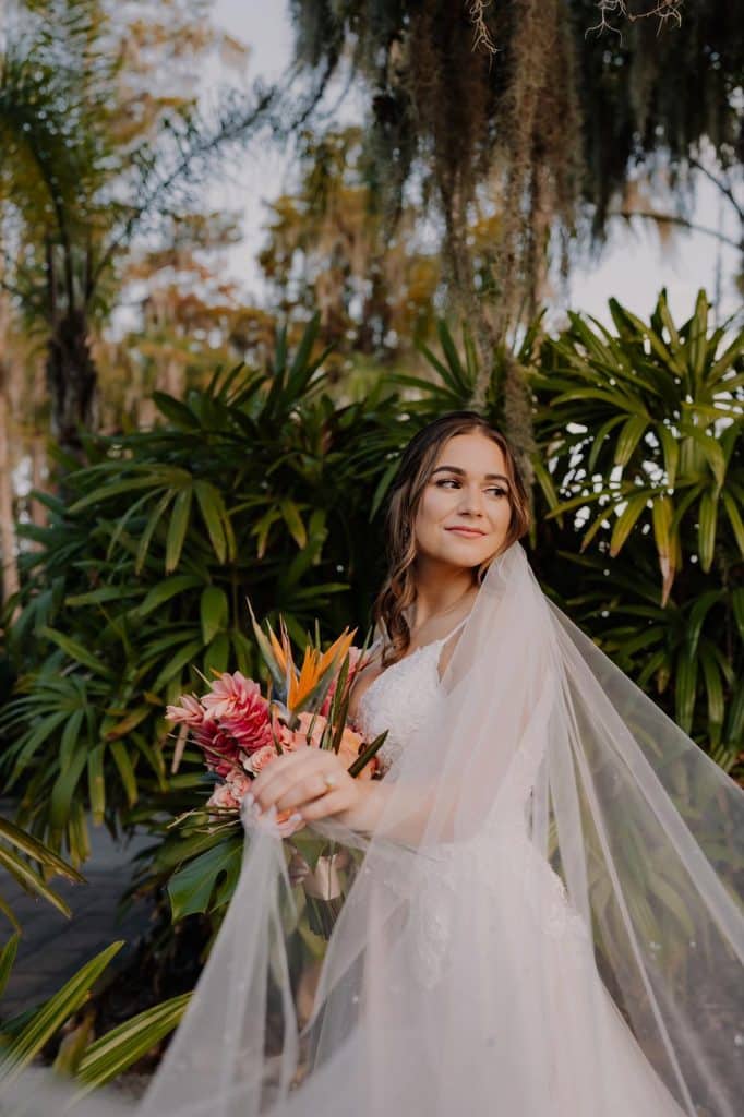 Bride posing with palm trees and willow trees behind her, with her sheer train extended out, Central FL