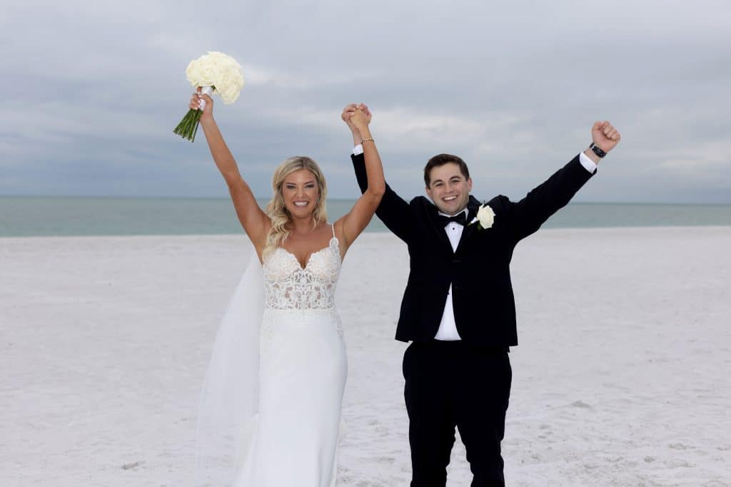 Bride and Groom standing on the sand at the beach, holding hands and raising them in celebration, JVK Photography, Central FL