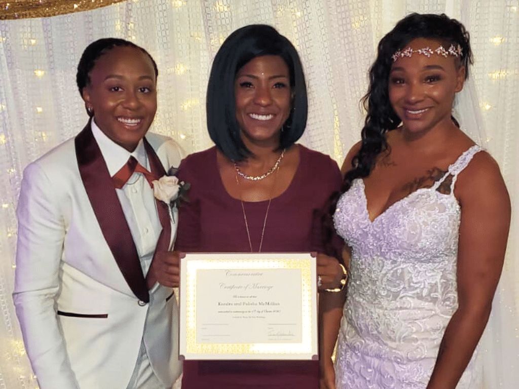 Married couple with their officiant holding their marriage certificate, white fabric with twinkle lights illuminated behind them, Central FL
