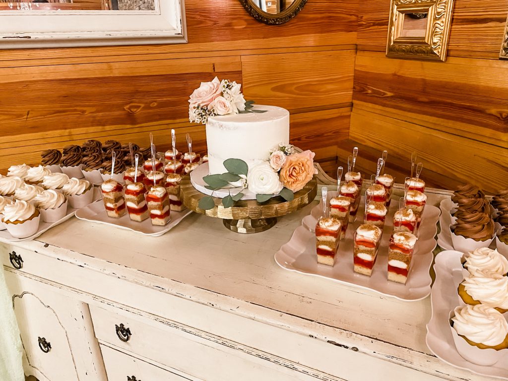Dessert served on a white wash dresser, with a one tiered cake adorned with pink flowers, dessert shooters and cupcakes on the sides, Central, FL