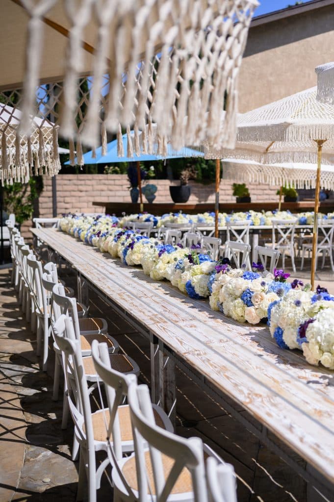 Long table for a special event, white chair rentals, white and purple flower centerpieces down the center, with umbrellas for sun coverage, Casear Event Rentals Orlando, Central FL
