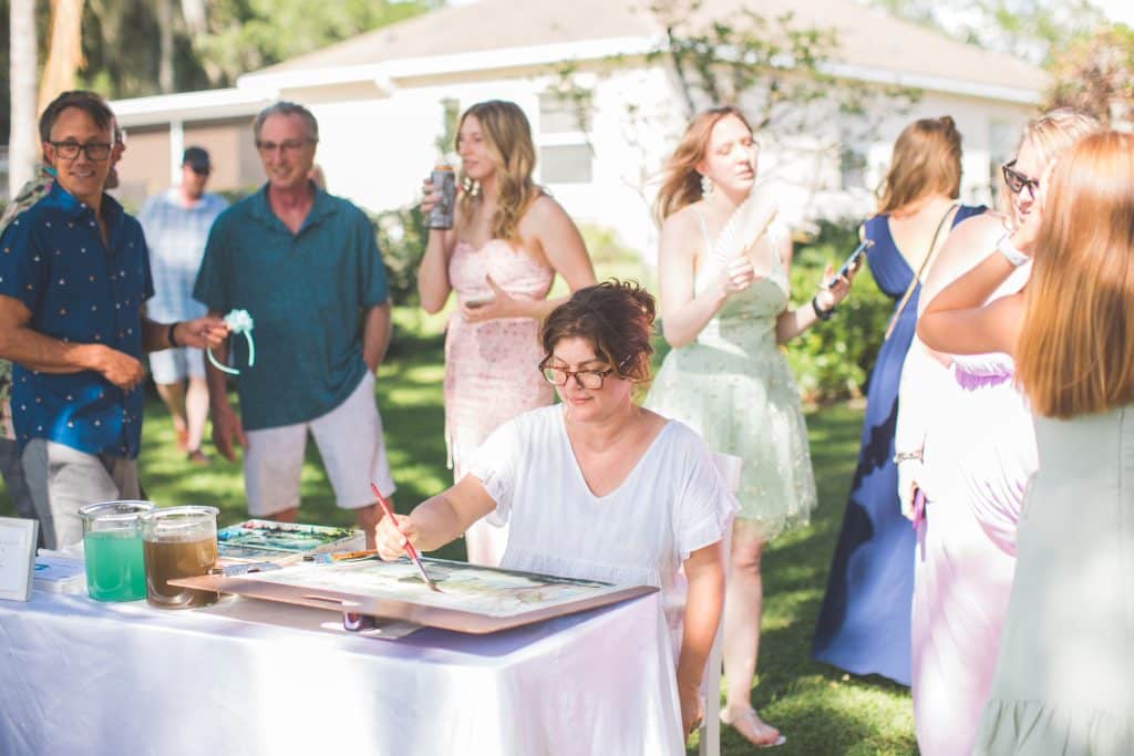 Caryn Dahm creating a watercolor painting at a wedding reception while guests mingle in the background, Central Fl